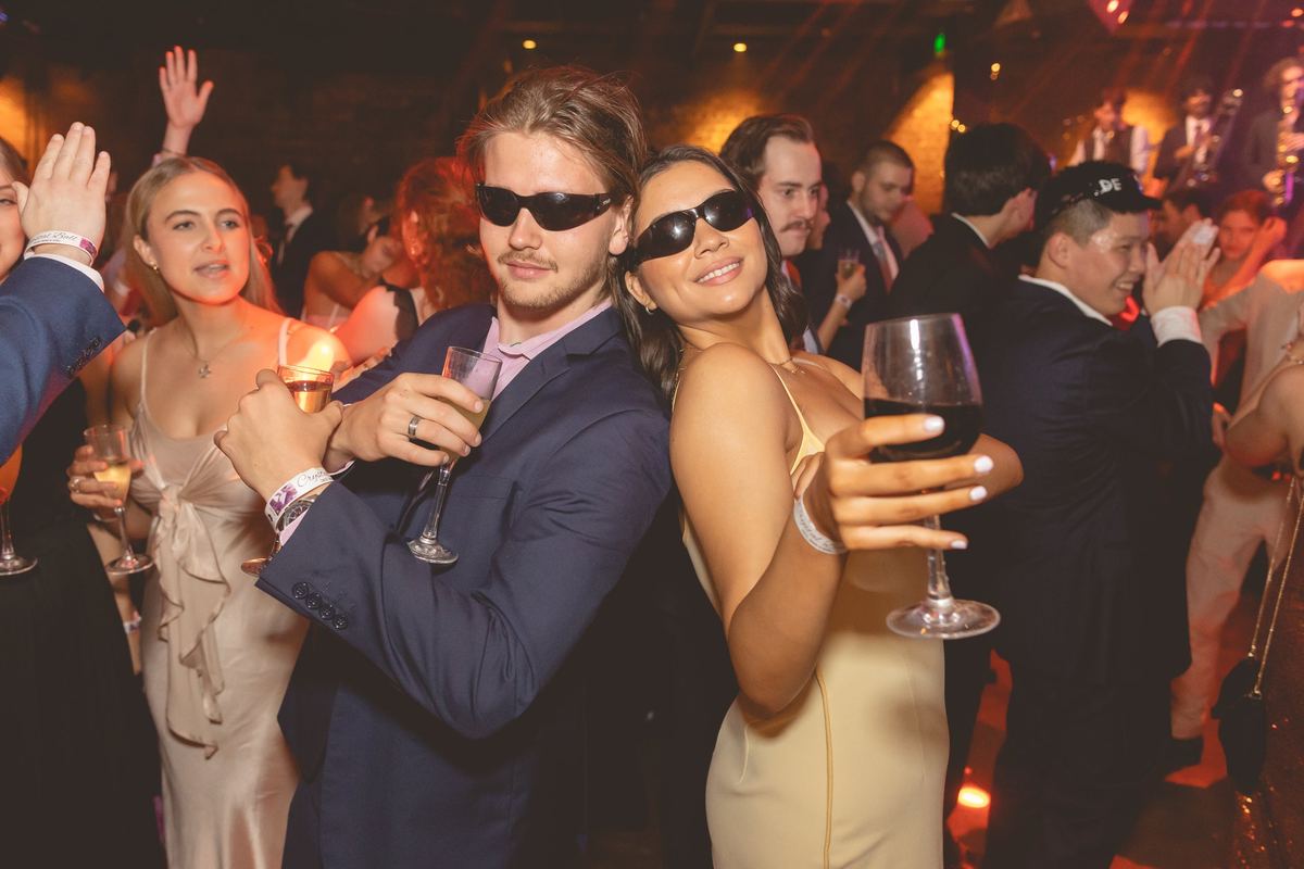 Two guests in sunglasses posing back to back with drinks in the middle of a crowded dance floor