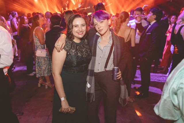 Two friends with their arms around each other on a busy dance floor, orange stage lights behind them