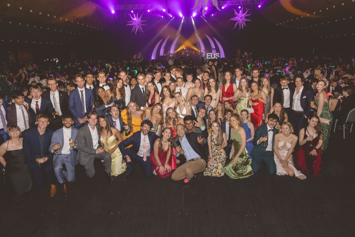 A large crowd of guests in formal wear gathered for one group photo in front of the stage at a ball
