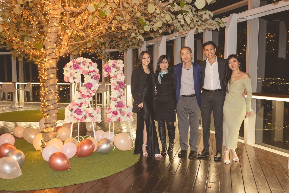Five guests beside 21 letters made of pink and white flowers on a rooftop terrace at night