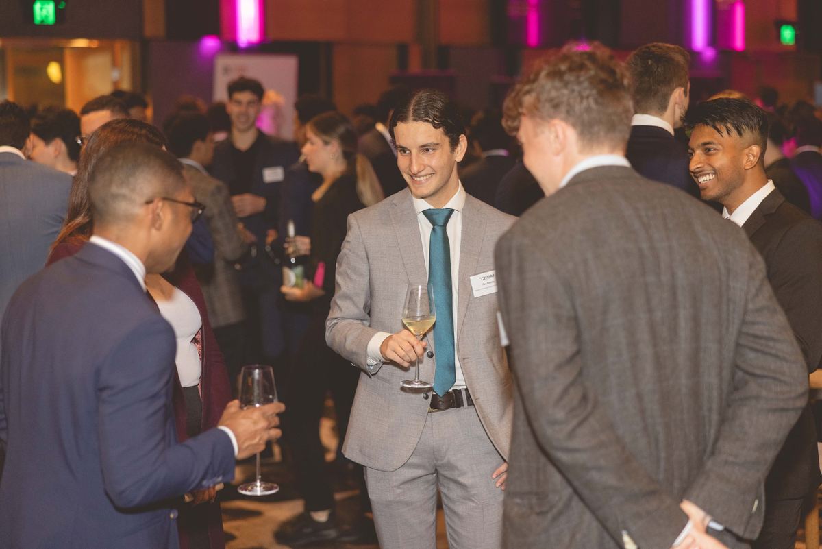 Guests in suits chatting with wine glasses at a busy evening networking event