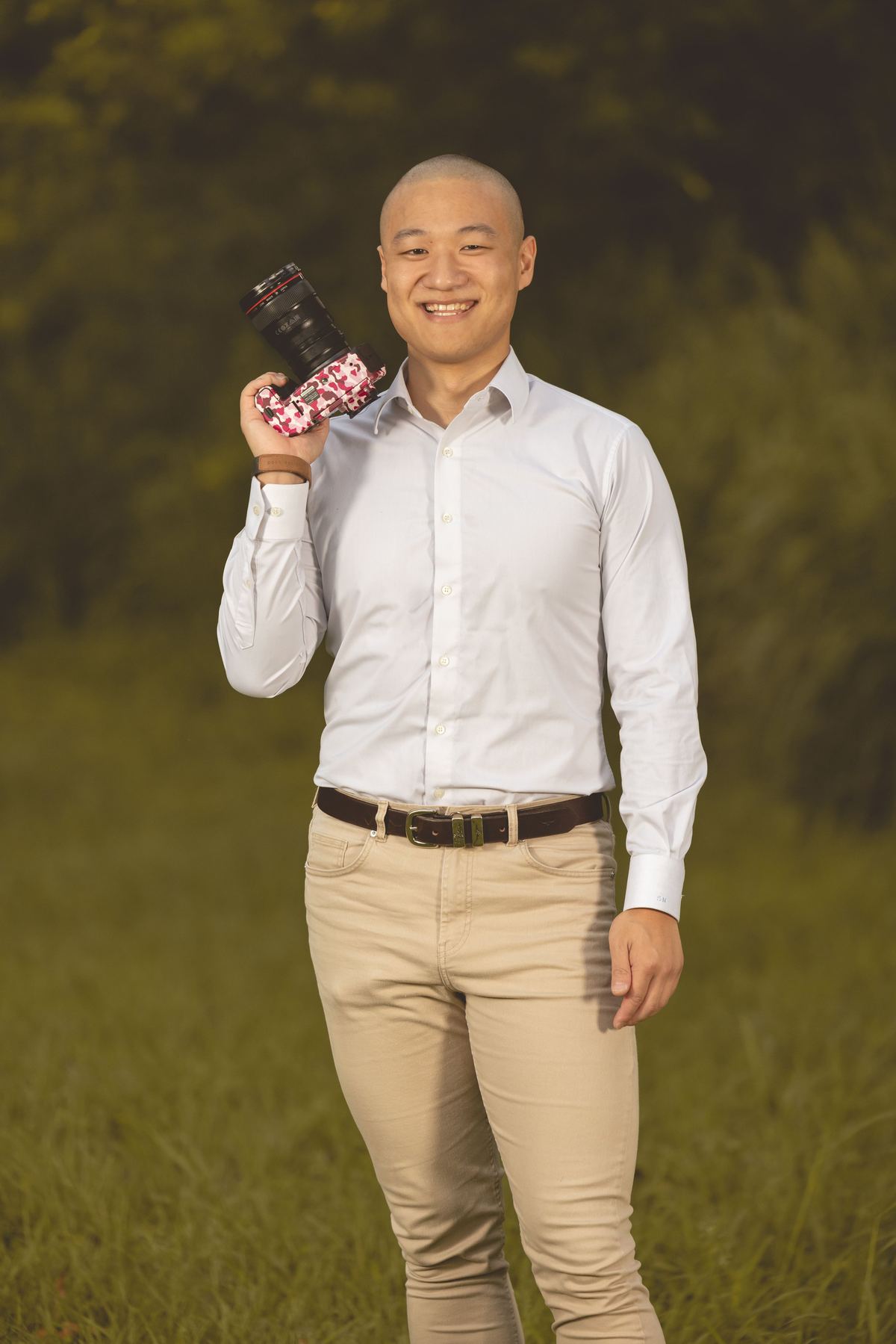 A photographer in a white shirt holding a camera, standing on grass in the evening