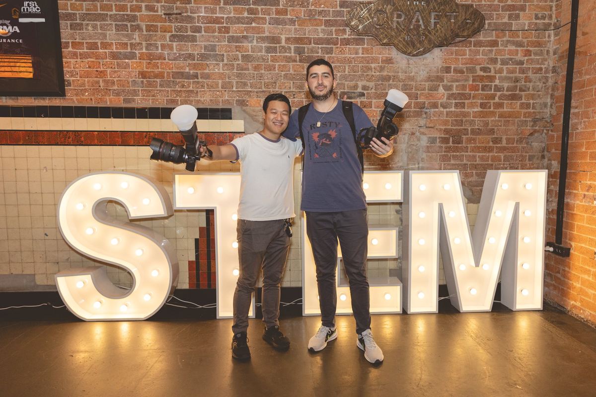 Two photographers holding up cameras with flashes in front of giant light-up letters