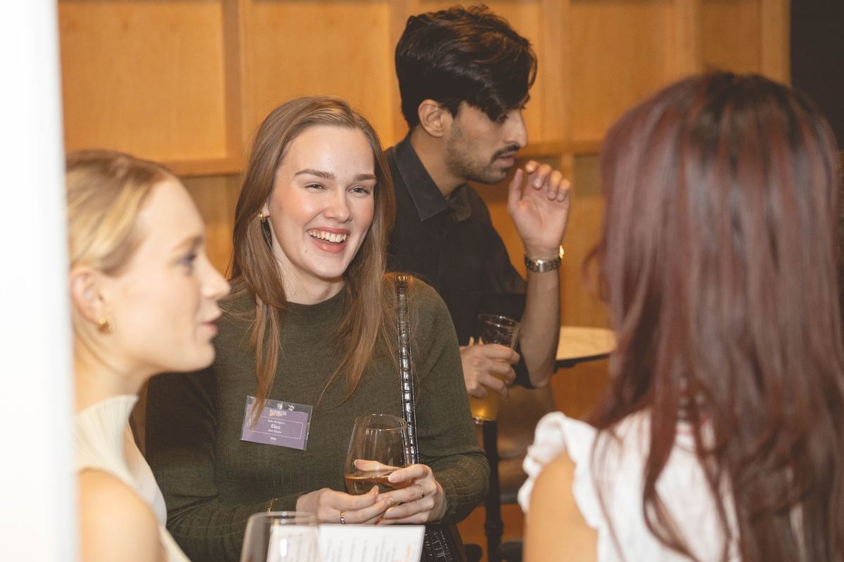 A guest with a name badge laughing mid conversation with friends at an evening event