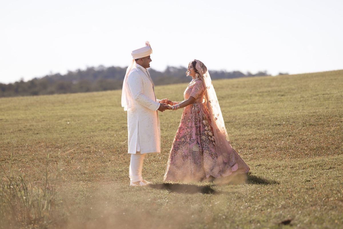 A bride and groom holding hands on an open grassy hill in the late afternoon