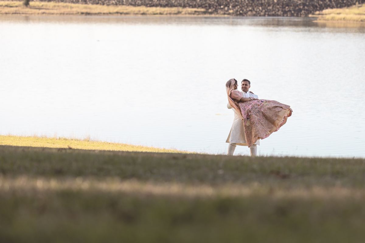 A groom lifting his bride so her gown swirls out beside a still lake